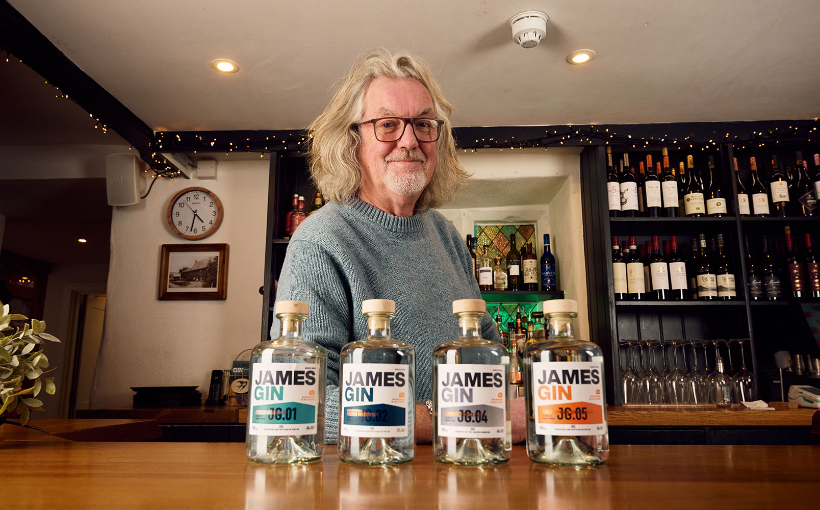 James May in his pub standing at the bar behind his range of four gin bottles