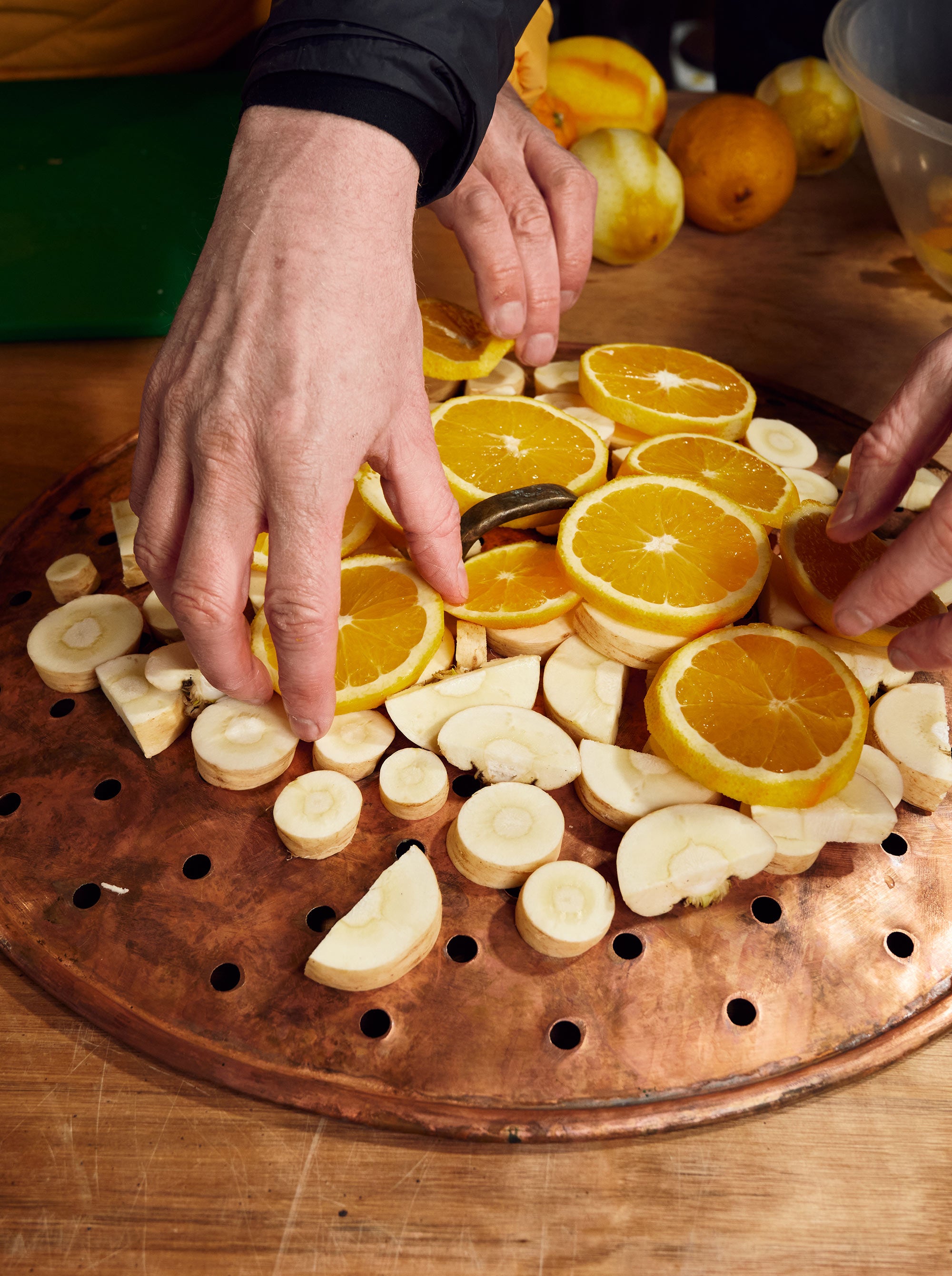 Hugh and James' hands arranging the botanicals orange and parsnip slices on a brass board