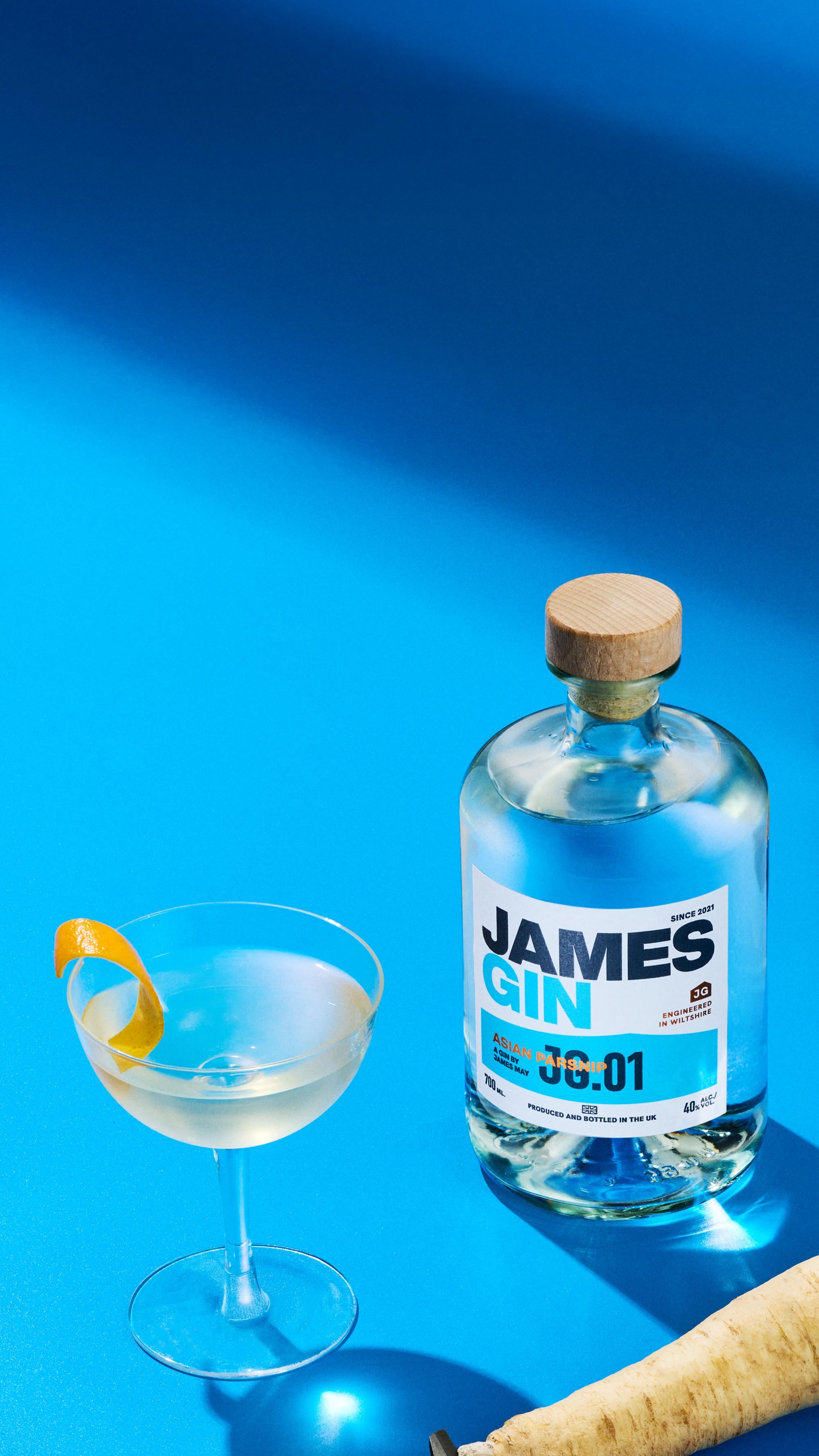 James Gin Asian Parsnip bottle developed by James May, with a cocktail and ingredients on a blue background