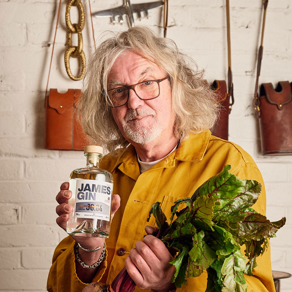 James May holding a bottle of his James Gin London Drizzle and a beetroot – premium gin by James May, produced and bottled in the UK.
